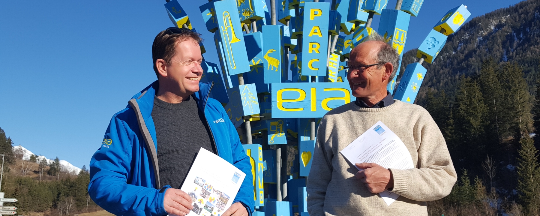 Geschäftsführer und Präsident des Vereins Parc Ela, Dieter Müller und Paolo Giacometti, mit Parkvertrag und Managementplan vor der Parc Ela-Skulptur in Tiefencastel. © Verein Parc Ela
